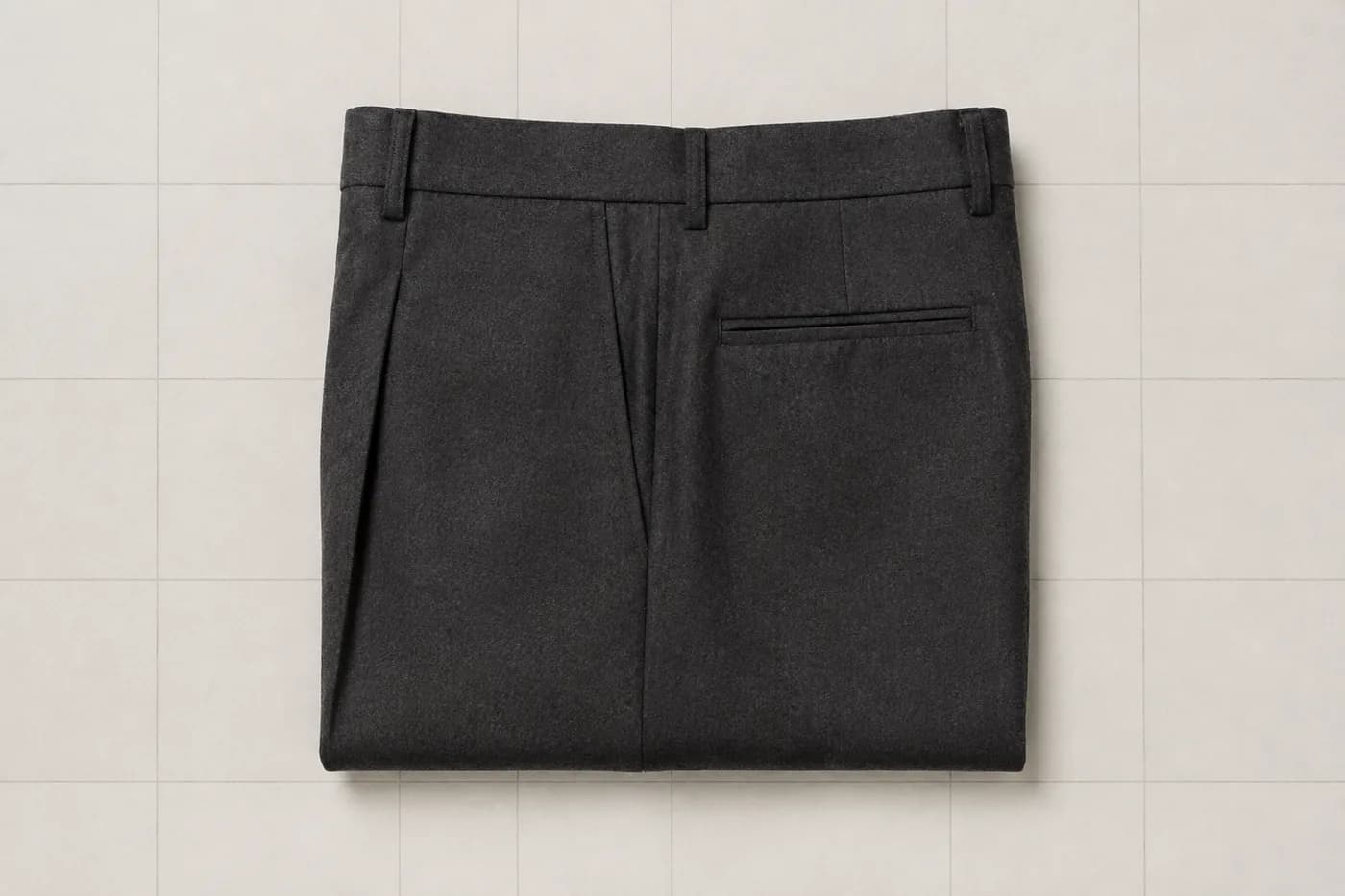 Charcoal wool trousers folded into a rectangle with a pressed crease.